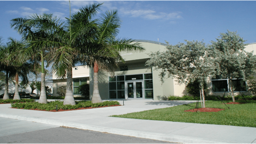 portrait of Miami Animal Import Center building surrounded by palm trees against a sunny blue sky