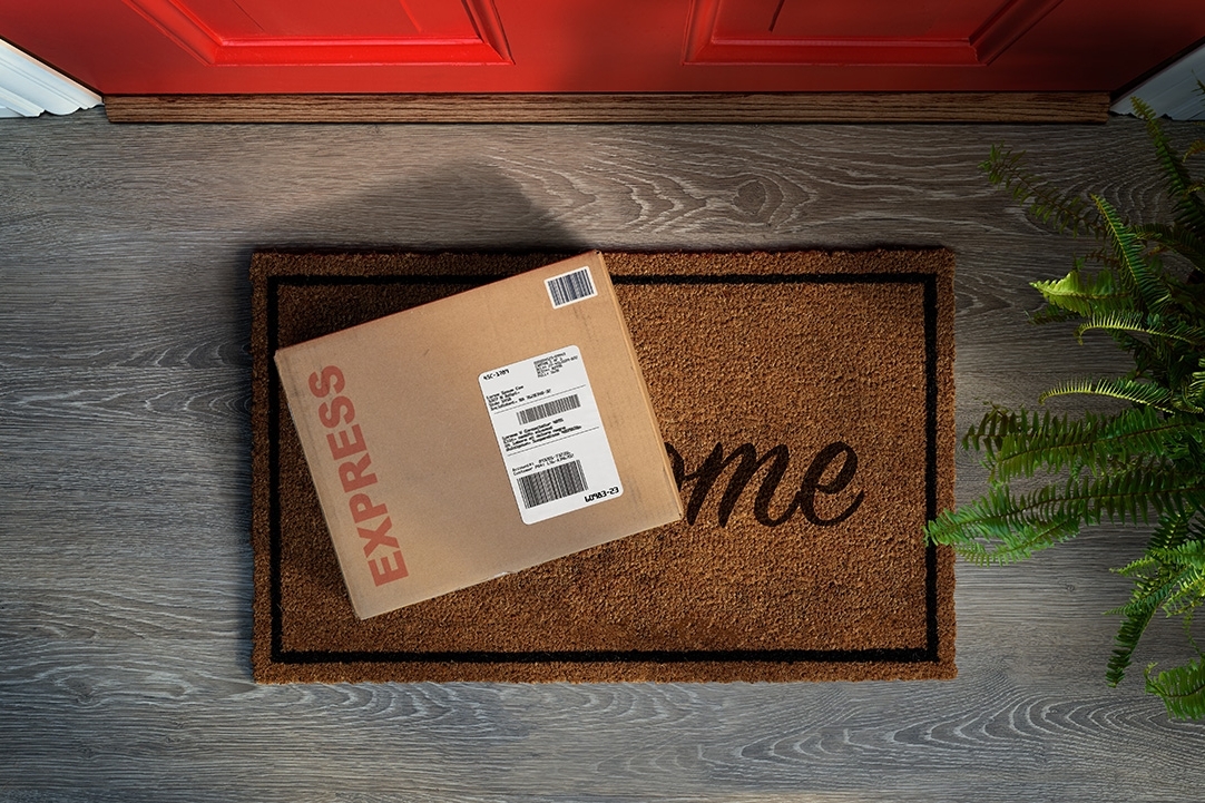 An express courier delivery box rests on a welcome mat outside a front door. (Overhead view.) 