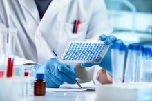 Scientist looking at samples panel microplate and writing down the data result of ELISA analysis