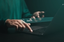 Close up image of a person typing on a computer with an internet search box graphic in the background