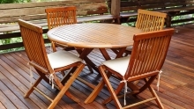 round teak table and four wood chairs with seat cushions on terrace